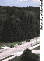 Photo. Photo image captured by traffic cameras of three cars on a highway. A red box highlights each of the cars moving through the scene and a blue circle highlights a pedestrian crossing in the center of the frame.