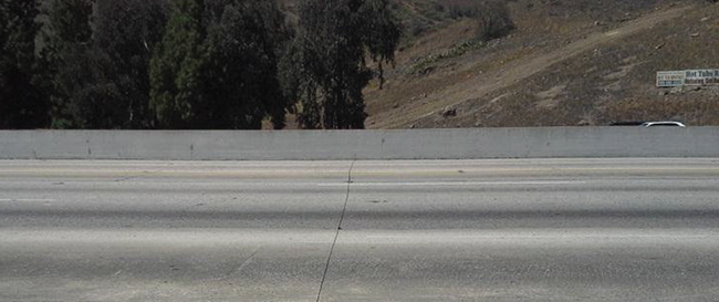 Photo of pavement slabs of Interstate 10 near Los Angeles, also called the San Bernardino Freeway. The roadway surface shows wear and damage, including joint deficiencies and spalls.