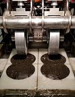Photograph. A machine prepares to roll two metal wheels onto two samples of a hot-mix bio-binder.