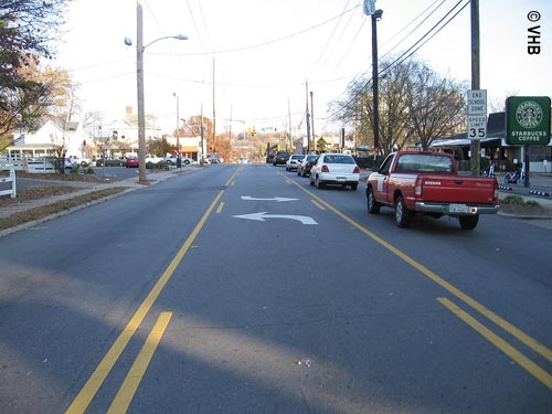 View of traffic on a three-lane street, with a pick-up truck and three cars in the right lane and no traffic in the left lane or the center lane, which has both left- and right-turn white arrow markings. A "Speed Limit 35" sign is posted, and street lights and utility poles are visible.