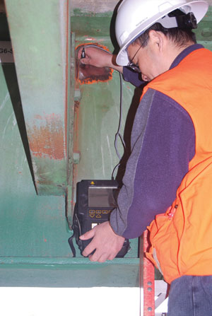 A worker in safety helmet and vest is using the Eddy Current bridge evaluation system on a metal structure.