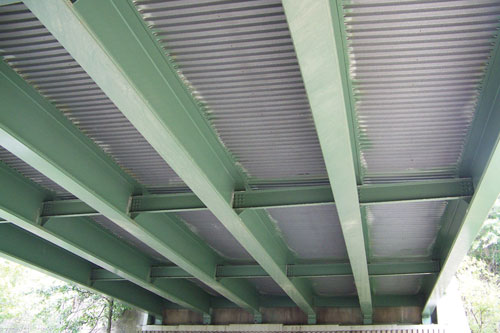 The underside of a bridge is shown with green-painted girders.