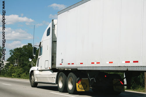 Side view of a white tractor trailer traveling on the outside right lane of a highway.