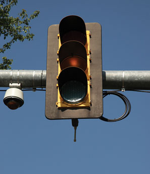 Close-up view of a traffic signal mounted on a gantry with a CCTV camera mounted to the left of the signal.