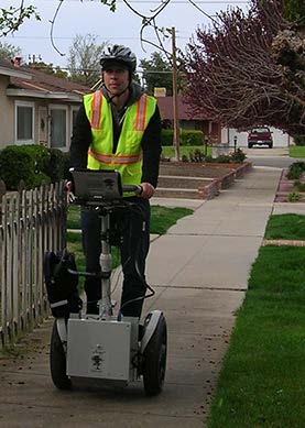 A stock photo shows a worker using a Segway, the Ultra-Light Inertial Profiler-ADA, to conduct an American with Disabilities Act (ADA) evaluation of sidewalk.