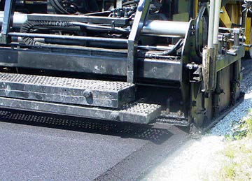 A stock photo shows a machine edging a segment of new pavement with the Safety Edge, consolidating the edge of a pavement to 30 degrees.