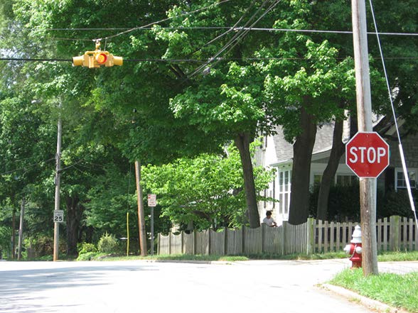 Stock photo shows an intersection in a residential area. An overhead flashing beacon controls the intersection along with a stop sign.