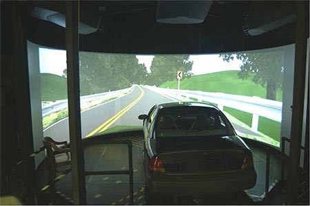 Photo of the Highway Driving Simulator at Turner-Fairbank Highway Research Center with an image of a two-lane road with guardrail on the screen