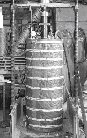 This photo shows the actual test setup depicted in figure 19. A large cylindrical soil mass inside a latex membrane is surrounded by the test apparatus to measure plunger load and vertical deformation.