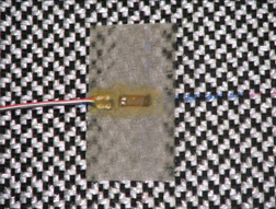 This photo shows a close-up of the strain gauge attachment technique used in the tests. The gauge is mounted on a lightweight nonwoven geotextile, and a microcrystalline wax and rubber coating was used.