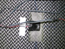 This photo shows a close-up view of the strain gauge attachment technique used in the tests. The gauge is mounted on a lightweight nonwoven geotextile, and a microcrystalline wax and rubber coating was used. Before placing the reinforcement sheet in the test specimen, tape was used to protect the gauges during compaction.