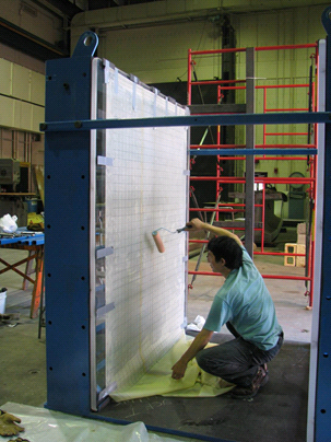 This photo shows a worker using a paint roller to attach at sheet of membrane at the bottom of the Plexiglas® surface inside the test bin.