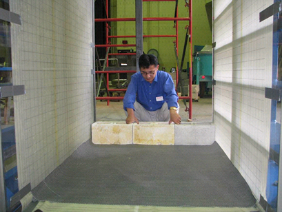 This photo shows a worker laying a row of modular concrete blocks between the walls and along the edge of the test bin.