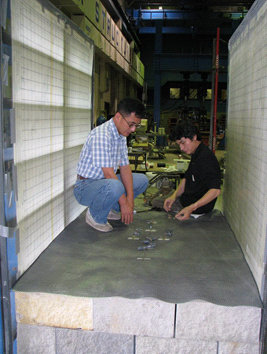 This photo shows two workers placing a layer of geosynthetic reinforcement across the top of the compacted fill and facing blocks.