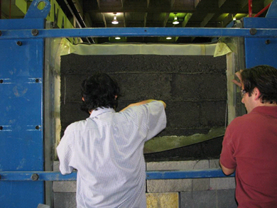 This photo shows two workers cutting off excess geotextile from behind the facing blocks.