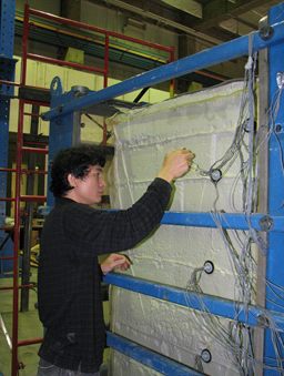 This photo shows a worker carefully applying epoxy between the cable and the membrane on the face of the test bin to prevent air leaks during testing.