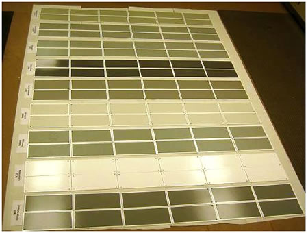 Figure 2. Photo. Composite of large panels. This photo shows the 6-by-12-inch (15-by-30-cm) panels. The panels are placed in 2-column sets, with each column consisting of 6 panels, making a total of 12 panels for each coating system. The individual coating systems are labeled below the columns. Panels are shown for all coating systems except glass flake reinforced polyester. All panels are covered with white tape around the edges and on the top in the center, where they are identified by numbers.