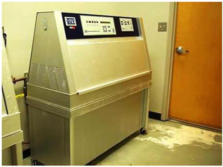 Figure 5. Photo. UV weathering tester. This photo shows an ultraviolet (UV) weathering tester, which is a large apparatus on four wheels. Test panels are loaded into the UV weathering tester from the sides. Test panel specimens are installed in the test machine so that they form the sidewalls of the test chamber. The chamber also consists of a water reservoir which is heated to produce the water vapor for condensation. The source of UV is light from 1.12 × 10-6 ft
(340 nm) lamps. Condensation and UV cycles are programmed using an automated controller. The unit has the capacity to shut off by itself at the end of the test cycle.