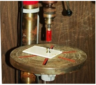 Figure 9. Photo. Drill press to score a test area around a dolly. This photo shows a test panel with a dolly affixed on the surface. Adhesion strength testing was performed by hydraulically pulling on test dollies affixed to the surface of test panels using an epoxy strength adhesive. A drill press with a bit scores around the dolly to isolate the adhesion test area.