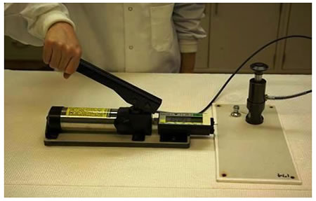 Figure 10. Photo. Hydraulic adhesion tester. This photo shows a hydraulic adhesion tester. The tester is a cylindrical enclosure that transfers the pumping action of the handle. The hydraulic force is transferred to a coupling fixture which attaches to the dolly to pull it away from the surface of the coating system.
