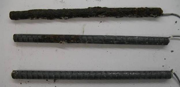 The top bar shows significant corrosion. The bottom bars (lower bars) also exhibit corrosion damage. In cracked concrete, significant amounts of corrosion products are observed on the top mat of conventional reinforcement, with nearly the entire surface area of the top mat of the steel showing corrosion. Corrosion on the bottom mat is limited to moderate sized regions; however, the corrosion on the bottom mat is significantly greater than that observed in uncracked concrete.