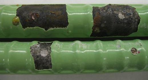 The bars were subjected to disbondment testing at locations that were intentionally damaged prior to the initiation of the corrosion test. The top bar shows significantly greater disbondment relative to the bottom bar, typical of all specimens on which a disbondment test was performed. Light corrosion products are observed at the damage site and under the disbonded area of epoxy on the top mat.