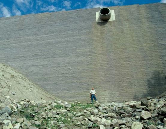 The photo  shows a man standing at the base of the Grand County, Colorado, geosynthetic  reinforced soil (GRS) wall that has a maximum height of 55 ft. The size of the  wall provides supporting evidence that the lateral pressures on GRS wall facing  are less than values estimated using classical earth pressure theory.