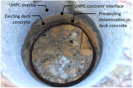 Figure 14. Photo. Photo of B7 test location after core removal.(2) This figure shows a photo of the B7-11 core location after testing and removal of the test specimen. The UHPC overlay material appears to be bonded well to the existing deck concrete. This is evident because cracks do not exist at the UHPC–concrete interface. A preexisting delamination in deck concrete is apparent.