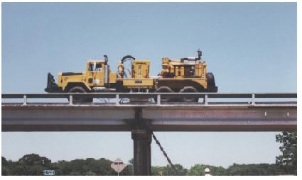 Vibroseis truck over Woodville Road Bridge pier. This image shows the Vibroseis truck parked on the bridge. The large truck has a servo-hydraulic vibrator mounted on its load bed. The photo is taken from the street that passes under the bridge at a sightline slightly below bridge level.