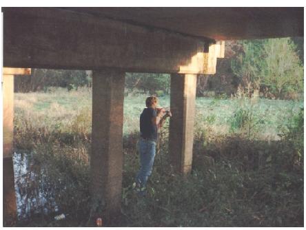 Drilling concrete holes to mount seismic accelerometers on bent 2 of structure 4, Trinity River Relief Bridge. This image taken under the bridge shows a worker drilling small holes at bent 2 of relief structure 4 of the Trinity River Relief Bridge. The holes are for concrete anchors where seismic accelerometers are to be attached.