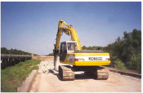 Demolition of structure 4, Trinity River Relief Bridge. This image, taken from the bridge roadway, shows a full-size tracked excavator machine with crane arm demolishing relief structure 4 of the Trinity River Relief Bridge in September 1997.