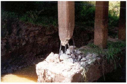 Bent and broken rebars of south column of bent 2. This image shows a closeup of the sheared south pile/column of bent 2, Trinity River Relief Bridge, with one of the four exposed number 8 steel rebars completely broken and the others bent. Ground water is visible under the strip footing.