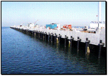 Figure 4. Photo. Fendering system in U.S. Navy Pier 10, San Diego, California. This figure is a color photograph of a large number of fender piles lining the outside of a very long pier. The fender piles are regularly spaced along the perimeter of the Navy pier. The fender piles depict an example of one experimental use of fiber-reinforced polymer composite piles.