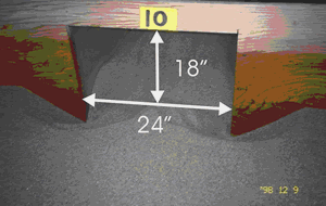 Figure 4. Rectangular model, vertical face. Photo. This picture shows a rectangular model of a bottomless culvert shape. The rectangle is 24 inches wide and 18 inches high, and it is surrounded by sediment that is lowest at the edges of the rectangle and peaks at its center. The sediment's highest point reaches 8 inches high, or 10 inches from the top of the rectangle.