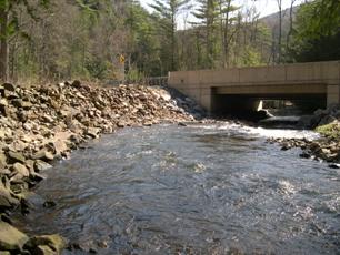 Figure 16. Riprap stabilization wall along Roaring Run, Pennsylvania. Photo. This photo shows a high riprap wall composed of graded riprap with a median size of about 152 to 229 millimeters. The purpose of the wall is to prevent lateral migration of the tight meander bend just upstream of the bridge.