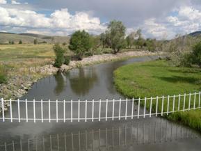 Figure 67. Cochetopa Creek, Rocky Mountains-upstream from bridge. Photo. This is looking upstream from the bridge. The channel clearly has been straightened and bank vegetation removed. Bank stabilization has been added on the right bank.