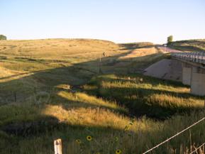 Figure 68. North Rush Creek, Great Plains-upstream of bridge. Photo. This is North Rush Creek in the Great Plains region looking upstream of the bridge. The stream winds through the plains; the bank vegetation consists of grasses. 