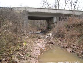 Figure 124. Unnamed creek (N 23), Atlantic Coastal Plain-looking upstream at bridge. Photo. This is looking upstream at the bridge. There is a drop at the end of the pad of several feet that is now being filled in with sediment.