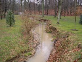 Figure 145. Kent County Tributary, Atlantic Coastal Plain-downstream from bridge. Photo. This is the Kent County Tributary in the Atlantic Coastal Plain region looking downstream from the bridge. Most woody vegetation has been removed for 91.5 meters downstream and replaced by grass. The bank lines are ragged due to mass wasting. 