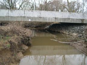 Figure 151. Morgan Creek, Atlantic Coastal Plain-looking upstream at bridge. Photo. This is looking upstream at the bridge. Mass wasting is evident on the right bank, and the left bank is stabilized with riprap under the bridge.