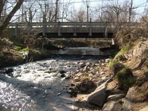 Figure 156. Hammond Branch, Atlantic Coastal Plain-looking upstream at bridge. Photo. This is looking upstream at the bridge. The collapsed bank stabilization material is seen in the channel bed.