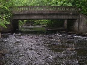 Figure 159. Pootatuck River, New England-looking downstream at bridge. Photo. This is looking downstream at the bridge. The channel is slightly shifted to the left as it passes under the bridge, and a bar is forming on the right side under the bridge.