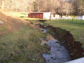 Figure 181. Wolf Run, Appalachian Plateau-upstream from bridge. Photo. This is Wolf Run in the Appalachian Plateau region looking upstream from the bridge. Bank vegetation is only grass. Significant bed degradation and bank widening is evident. 