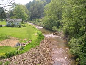 Figure 194. Piney Creek, Appalachian Plateau-upstream from bridge. Photo. This is looking upstream from the bridge. Bank vegetation is grass on the right bank and thick brush and trees on the left bank. A large point bar is deposited on the right bank just upstream from the bridge. 