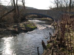 Figure 211. Indian Run, Piedmont-looking downstream at bridge. Photo. This is looking downstream at the arch bridge. Fiber logs have been placed on the right bank in an attempt to prevent lateral migration. The channel has migrated against the right abutment of the bridge.