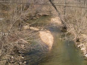 Figure 213. Middle Patuxent River, Piedmont-upstream from bridge. Photo. This is the Middle Patuxent River in the Piedmont region looking upstream from the bridge. Bank vegetation consists of moderately dense trees and shrubs. A midchannel bar is in the channel. 