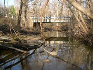Figure 220. Atherton Tributary, Piedmont-looking downstream at bridge. Photo. This is looking downstream at the bridge. The channel is well-aligned with the bridge. There is considerable debris accumulation upstream of the bridge.