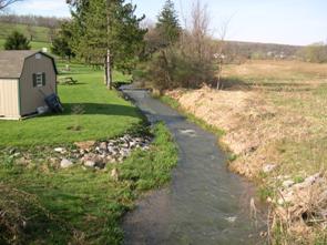 Figure 229. Buffalo Run, Valley and Ridge-upstream from bridge. Photo. This is the Buffalo Run in the Valley and Ridge region looking upstream from the bridge. Few trees are on the banks. The remaining vegetation is grass. The right bank has experienced erosion, and some riprap bank stabilization is in place. The channel appears to have been straightened.