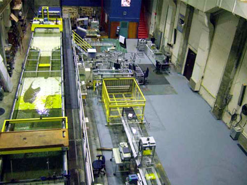 Figure 1. Photo. View of the flume in the Hydraulics Laboratory. The photo is an overhead view of the flume in which the bottomless scour experiments were conducted. The flume is located on the left side of the photo. The flume’s long dimension, or length, rises from the bottom of the photo to the top. A flume for other experiments is in the center of the photo. The right side of the photo shows one wall of the laboratory room.