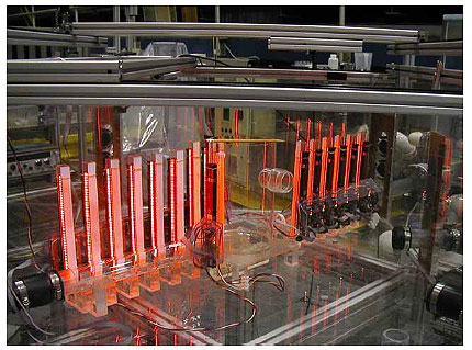 Figure 5. Photo. The scaled model of an access hole equipped with standpipe instruments. This photo shows a Plexiglas model of an access hole with level Plexiglas inlet and outlet pipes near the bottom. The pencil resting on top of the access hole shows that the access hole model is smaller in diameter than the pencil and is perhaps two pencils, or approximately 0.305 meters (1 foot), deep. The inflow and outflow pipes are equipped with small Plexiglas standpipes that are positioned at equally spaced intervals along their length. The standpipes connect to the bottom of the inlet and outlet pipes such that water can enter each standpipe. The level of water in each standpipe is measured by an electronic CIS instrument.